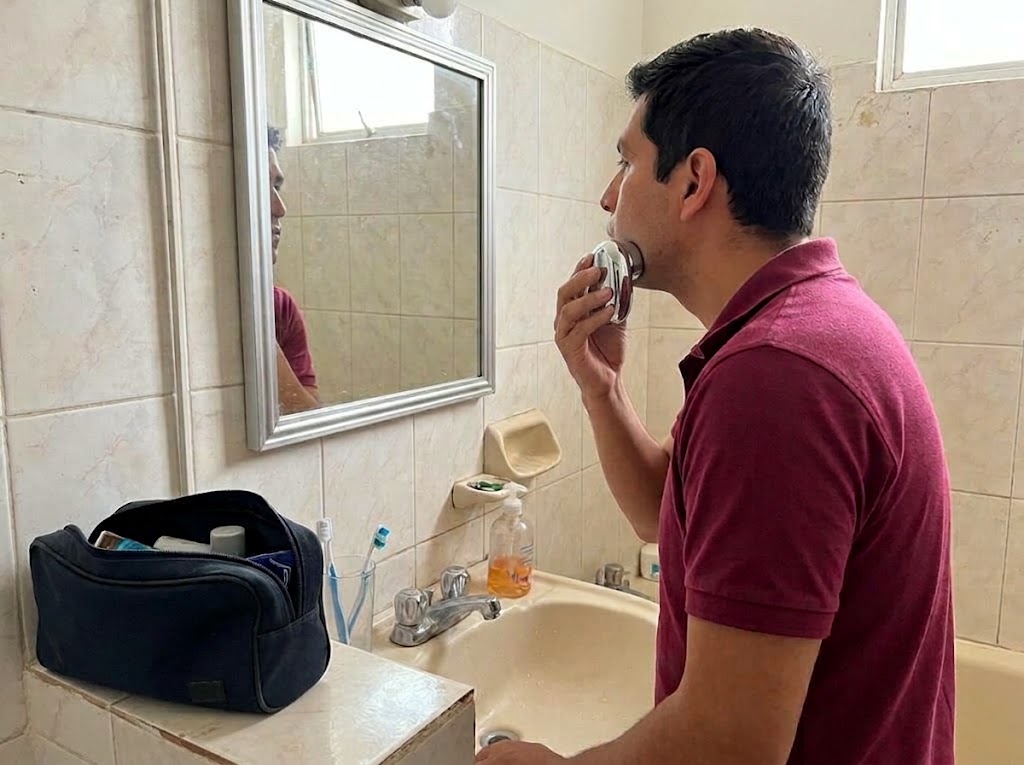 Hombre afeitándose frente al espejo con la afeitadora portátil
