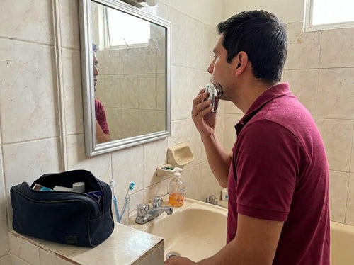 Hombre afeitándose frente al espejo con la afeitadora portátil